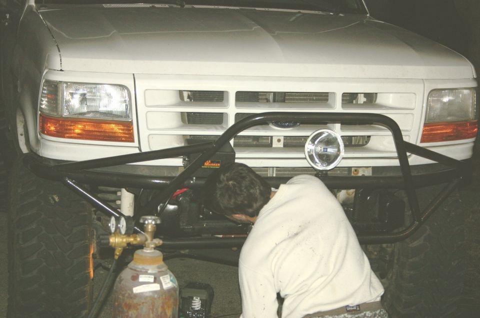 White 1995 Ford Bronco front end with custom bumper and a person welding