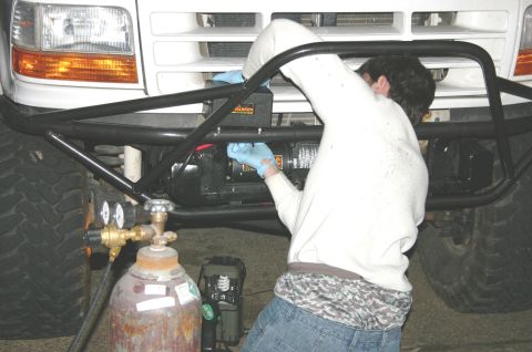 1995 Ford Bronco - A person in blue gloves works on a winch attached to the front of a truck, with a gas cylinder nearby.
