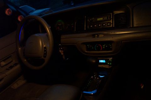 1999 Ford Crown Victoria - Nighttime interior shot of a Ford sedan showing the steering wheel with center airbag, illuminated green gauge cluster, center stack with r…