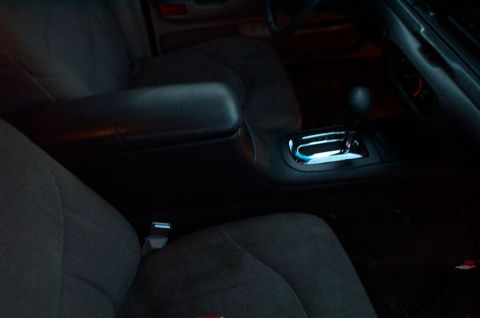 1999 Ford Crown Victoria - Dimly lit interior of a car showing the front seats, center console with padded armrest, and an illuminated automatic gear selector with ch…