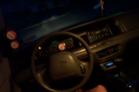 1999 Ford Crown Victoria - Nighttime interior shot from the driver's seat of a Ford sedan, showing the gray steering wheel with Ford emblem, illuminated instrument cl…