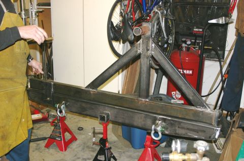 1995 Ford Bronco - A person in a yellow apron works on fabricating a custom rear bumper and tire carrier assembly in a garage.