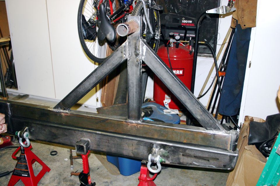 Custom fabricated steel rear bumper with tire carrier mount, supported by red jack stands