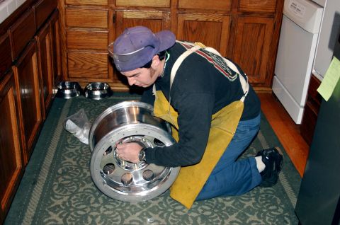 1995 Ford Bronco - A person is kneeling and inspecting a large, polished metal wheel, possibly for a truck or heavy equipment.