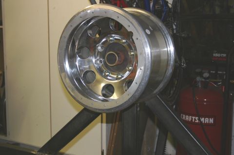 1995 Ford Bronco - A polished chrome wheel with eight visible lug nuts is mounted on a metal stand, with an air compressor and other equipment in the backgrou…