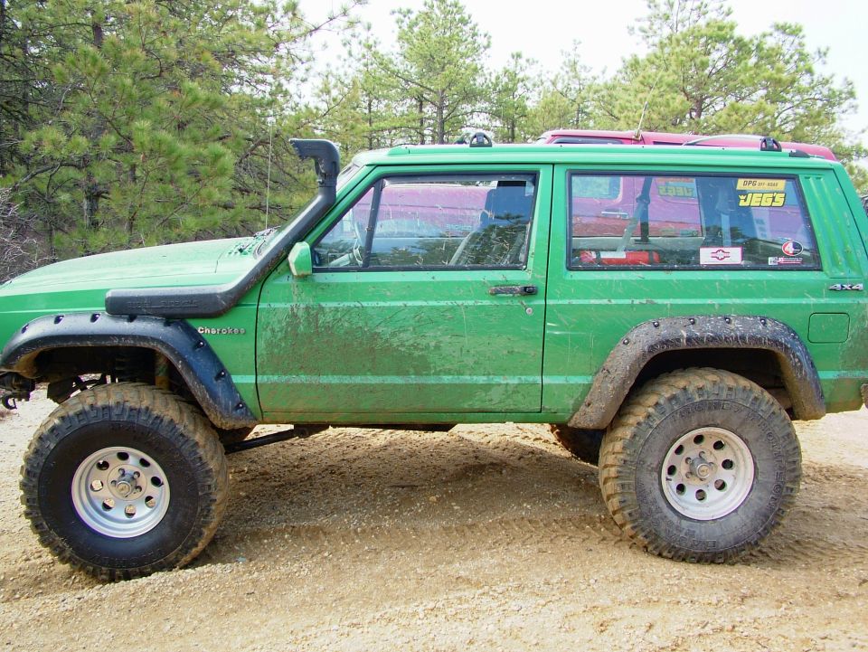 Green Jeep Cherokee with snorkel, off-road tires, and roof rack, seen from the side