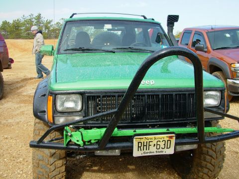 1994 Ford Bronco - This green Jeep Cherokee features a snorkel and a heavy-duty bull bar, parked alongside another vehicle.
