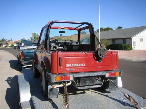 1987 Suzuki Samurai - A red 1987 Suzuki Samurai is seen on a trailer, with another vehicle towed behind it on a sunny day.