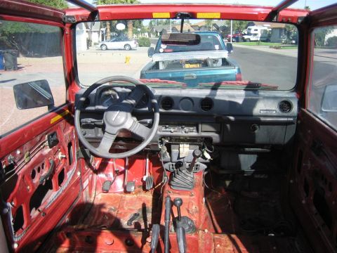 1987 Suzuki Samurai - The interior of a gutted 1987 Suzuki Samurai shows exposed red metal and a manual transmission.