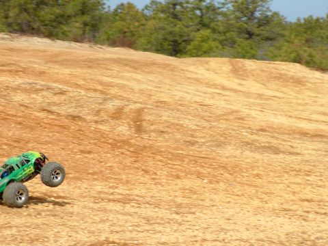 1994 Ford Bronco - RC monster truck jumps on a dirt track with trees in the background.