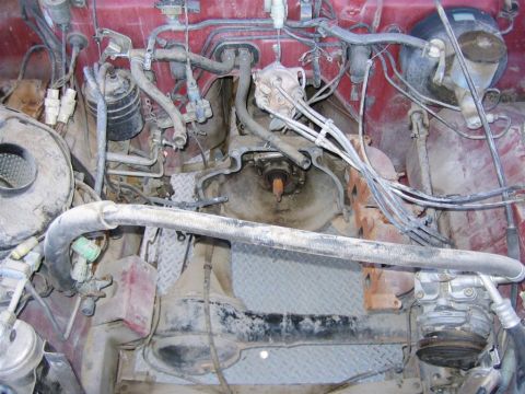 1987 Suzuki Samurai - The engine bay of a vehicle shows exposed mechanical parts, hoses, and wiring, with red paint on the interior.