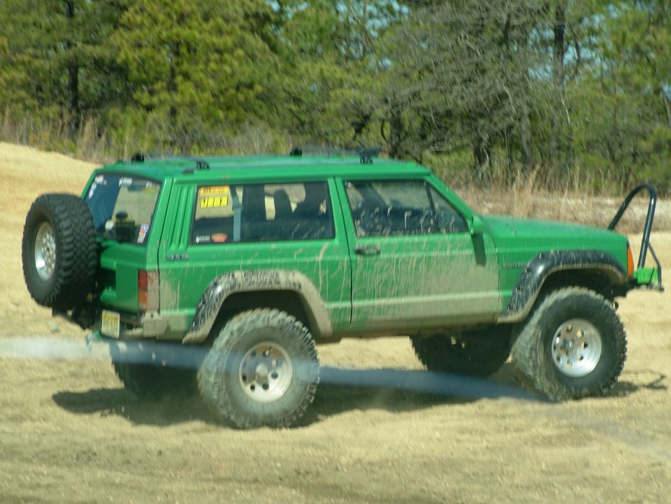 Green Jeep Cherokee XJ with spare tire on rear door and off-road tires