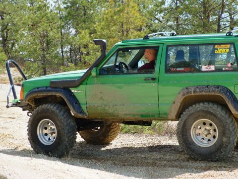 1994 Ford Bronco - Modified green Jeep Cherokee XJ with snorkel and off-road tires on a dirt path.