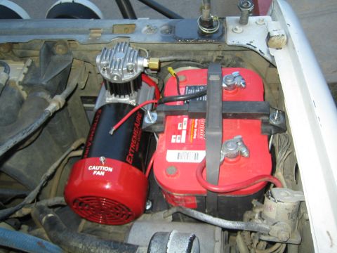 1990 Ford Bronco - engine bay shows a black ExtremeAire air compressor with a red Caution Fan guard mounted beside a strapped-down red battery.