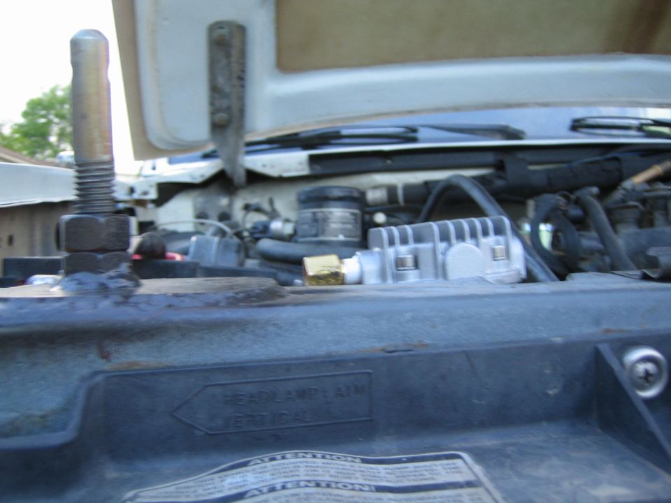 Under-hood view near a vehicle radiator support with an Attention warning label and shock tower