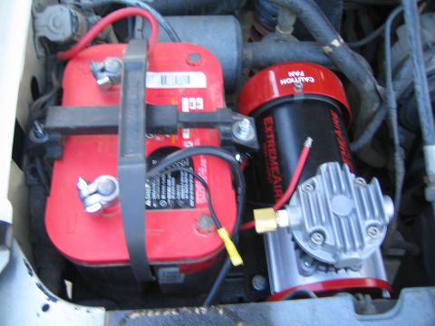 1990 Ford Bronco - engine bay holds two strapped red Optima batteries next to a black ExtremeAire air compressor with a Caution Fan guard.