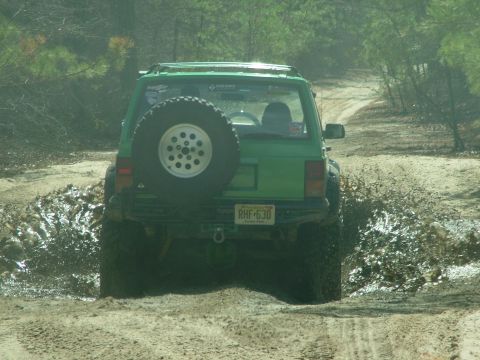 1994 Ford Bronco - This green SUV navigates a muddy trail, kicking up water and dirt as it drives.