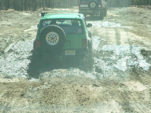 1994 Ford Bronco - Two SUVs navigate a muddy trail, kicking up water and dirt.