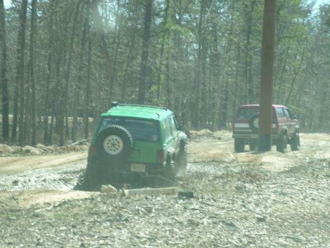 1994 Ford Bronco - Two SUVs navigate a muddy, wooded trail with one vehicle partially stuck.
