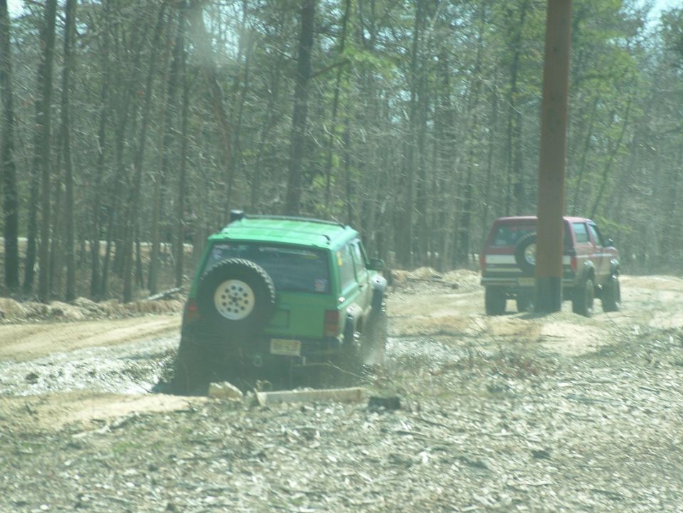 green SUV stuck in mud, red SUV behind it on dirt road