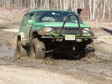 1994 Ford Bronco - Modified Jeep Cherokee XJ navigating a muddy trail, showing off its off-road capabilities.