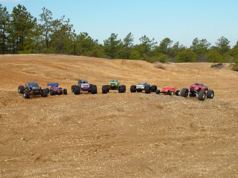 1994 Ford Bronco - Multiple remote control monster trucks are parked on a dirt terrain under a clear sky.