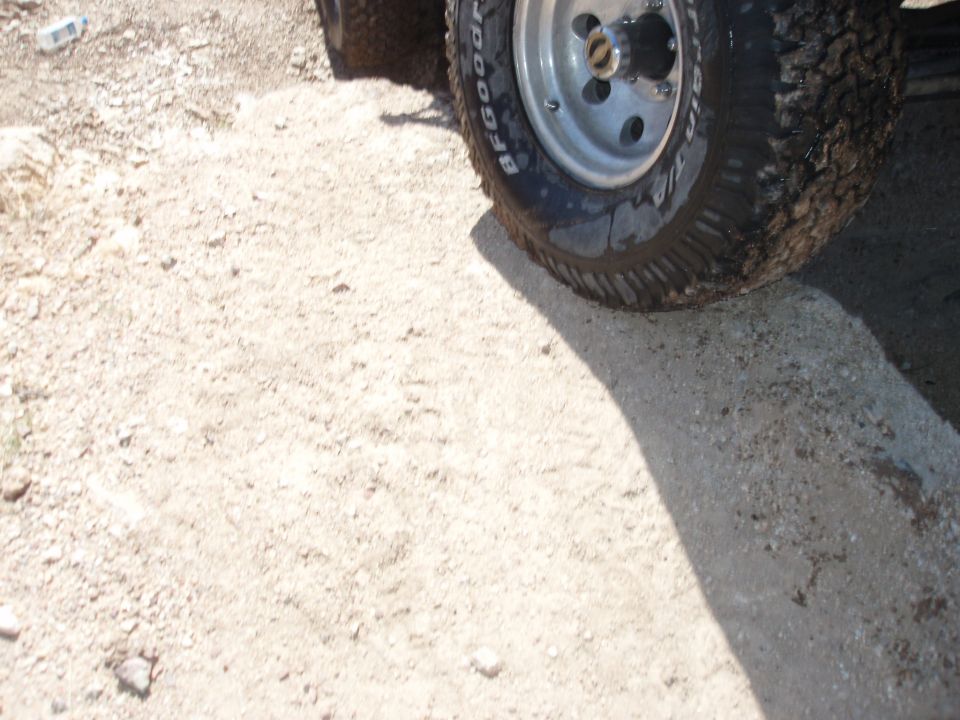 BFGoodrich All-Terrain tire on silver steel wheel, muddy, on rocky dirt ground