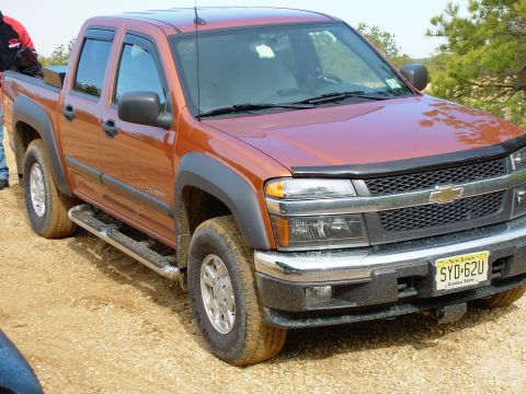 1994 Ford Bronco - Orange Chevrolet Colorado pickup truck with New Jersey license plate SYD-62U parked on dirt road.