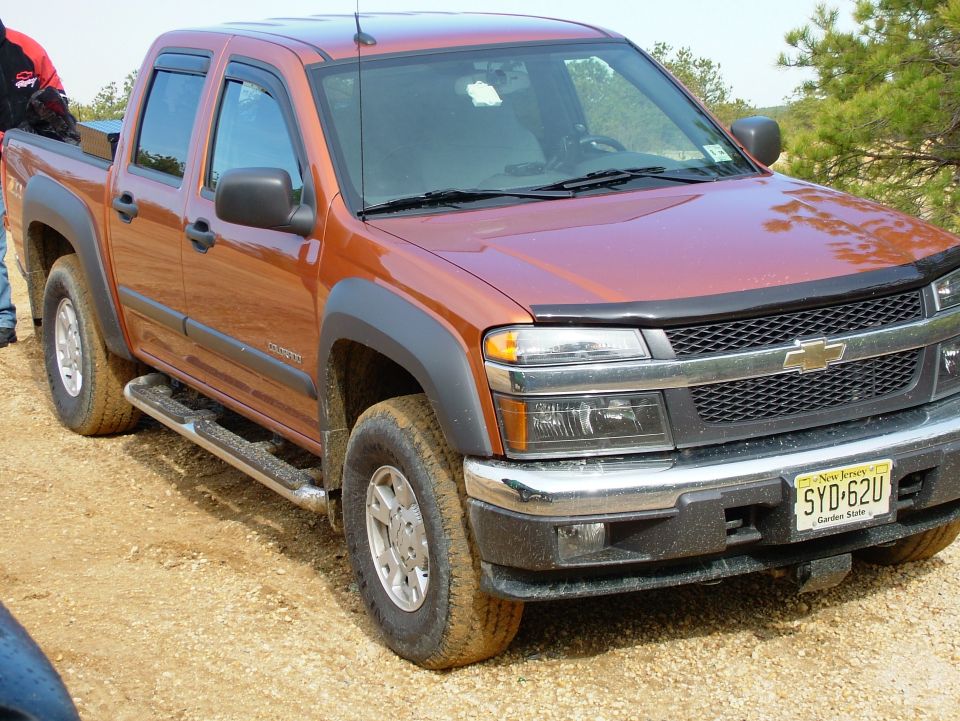 Orange Chevrolet Colorado pickup truck with New Jersey license plate SYD-62U parked on dirt road
