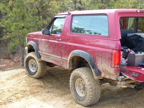 1994 Ford Bronco - This red Ford Bronco is covered in mud after driving on a dirt path.
