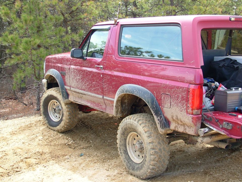 red Ford Bronco with large tires on dirt road, trees in background