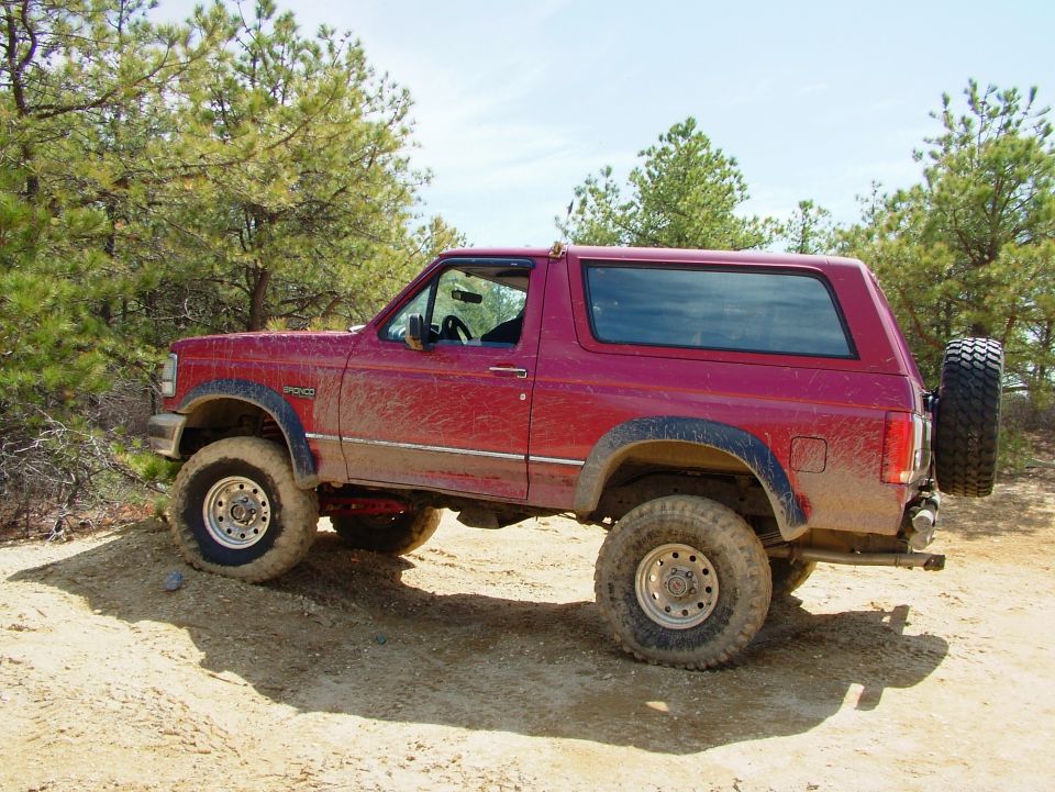 Red Ford Bronco with lifted suspension and off-road tires on a dirt path