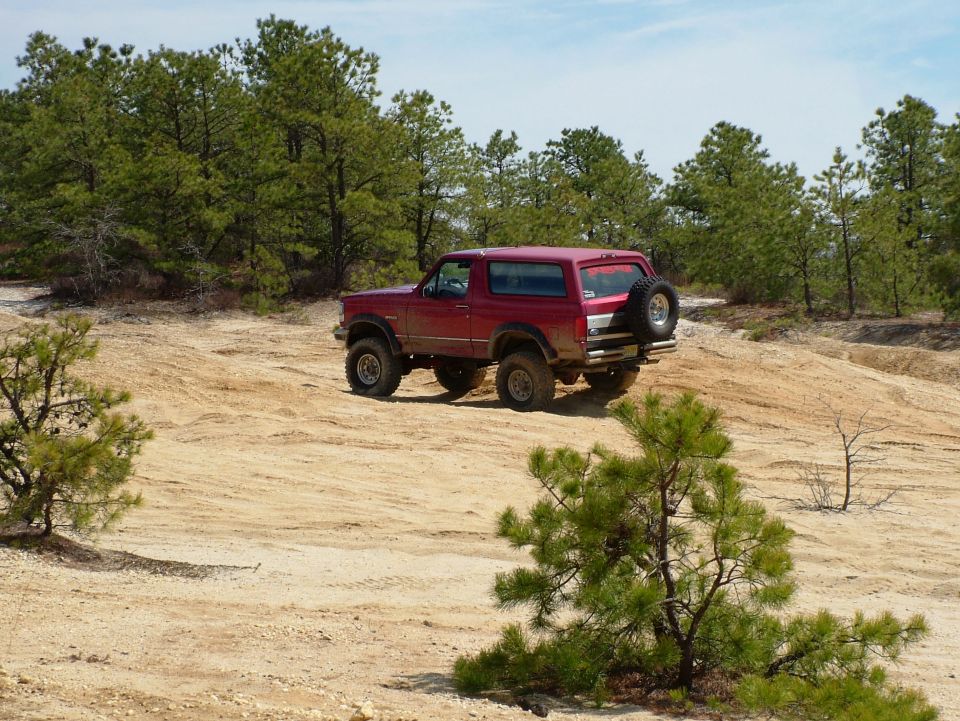 Red 1994 Ford Bronco driving on a sandy, wooded trail