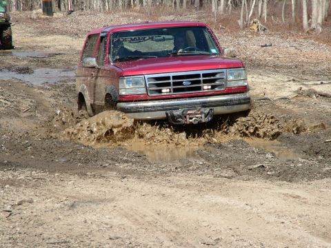 1994 Ford Bronco - Red 1994 Ford Bronco navigates a muddy trail, with another vehicle in the background.