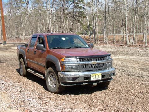 1994 Ford Bronco - This orange Chevrolet Colorado pickup truck is parked on a dirt road. The license plate is visible.