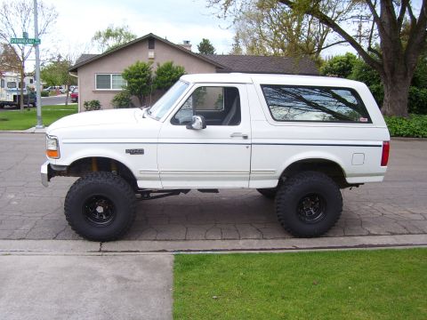 1994 Ford Bronco - A white lifted Ford Bronco is parked on a suburban street.