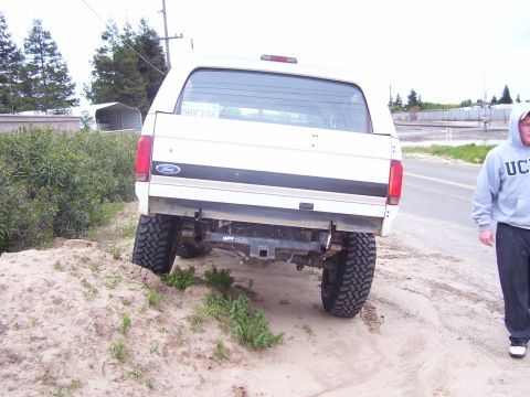 1994 Ford Bronco - A white Ford Bronco is parked on a dirt embankment next to a road, with a person walking away from it.