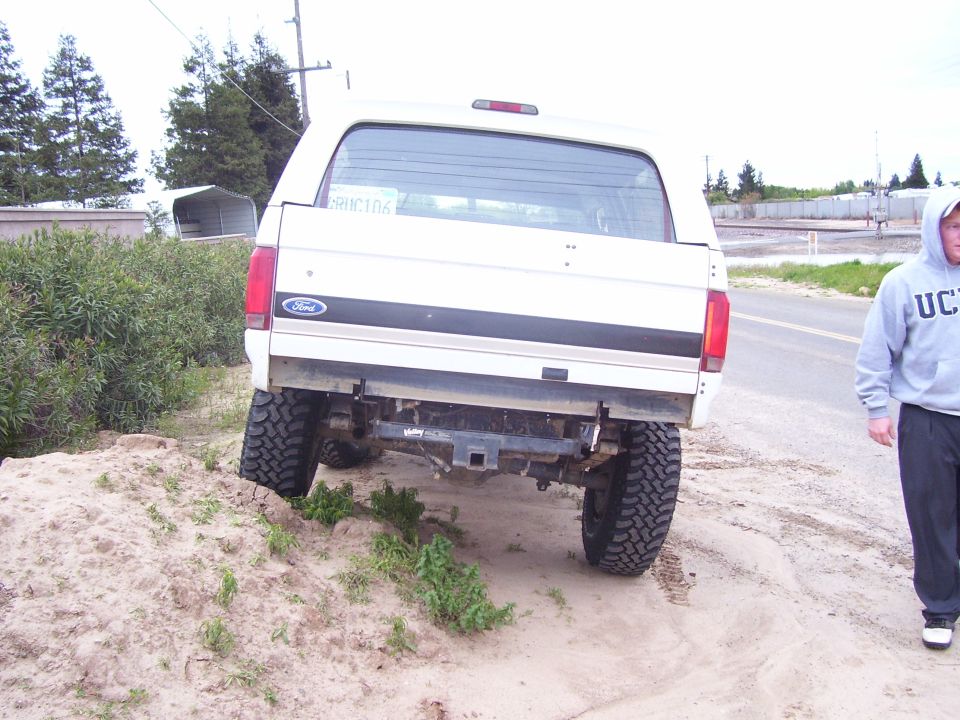 White Ford Bronco parked on dirt with a man walking nearby. License plate reads 'BRNC106'
