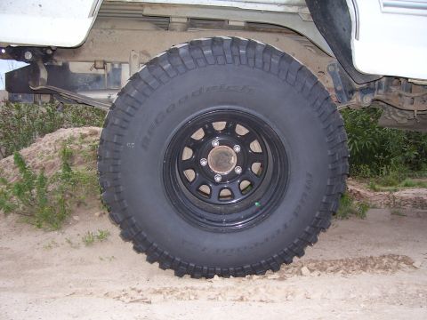 1994 Ford Bronco - A BFGoodrich Mud-Terrain T/A tire is visible on the rear of a white vehicle, with suspension components and sandy terrain in the background.