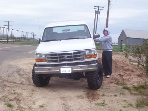 1994 Ford Bronco - A person stands next to a lifted white Ford Bronco with oversized tires.