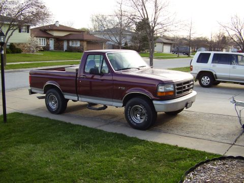 1996 Ford F-150 - A maroon Ford F-150 pickup truck is parked on a concrete driveway in front of a suburban house.