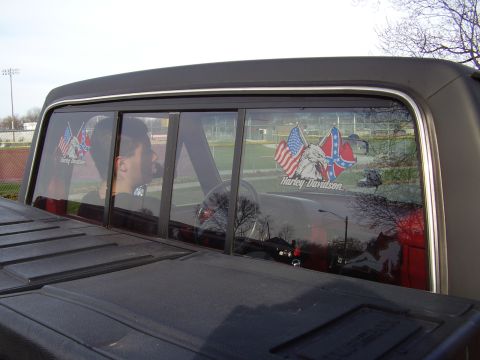 1996 Ford F-150 - Rear window of a truck displays patriotic and motorcycle-themed stickers, with a person visible inside.