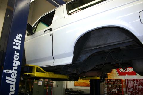 1995 Ford Bronco - A white SUV is raised on a lift, providing a clear view of its undercarriage and the rear wheel well area.