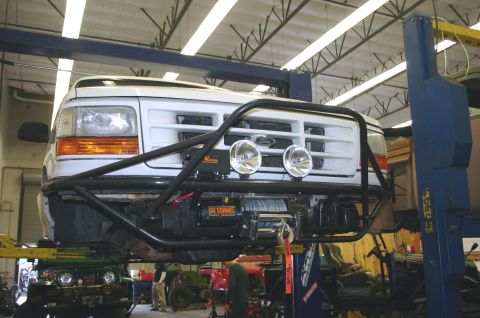 1995 Ford Bronco - White Ford Bronco with a custom bull bar and winch is lifted on a car hoist in a garage.