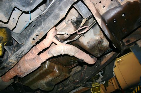 1995 Ford Bronco - The undercarriage of a vehicle shows the exhaust system and frame components, with a yellow car visible in the background.