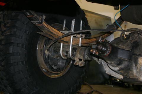 1995 Ford Bronco - Close-up view of a vehicle's rear axle assembly, leaf springs and a large off-road tire. The Supermotors logo is visible in the lower right…