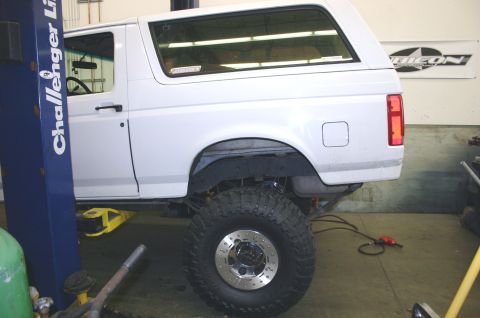 1995 Ford Bronco - This white SUV is elevated on a lift, its large off-road tires and suspension components.