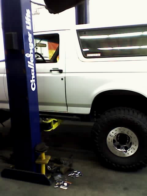 1995 Ford Bronco - A white SUV is raised on a hydraulic lift in a garage, with tools scattered on the floor.