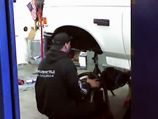 1995 Ford Bronco - A mechanic works on the suspension of a white Ford Bronco, which appears to be from the early to mid-1990s.