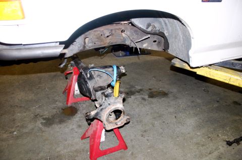 1995 Ford Bronco - A vehicle's front suspension assembly is supported by red jack stands, with the frame of a white vehicle overhead.